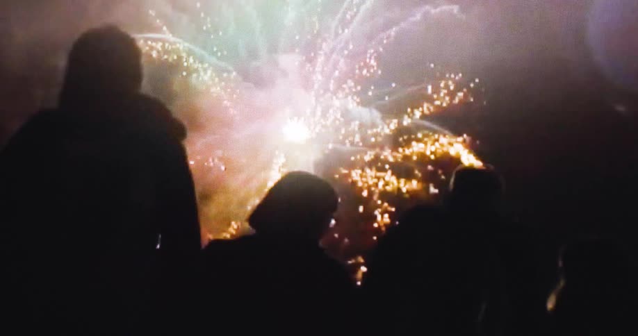 The crowd are watching a fireworks show at night