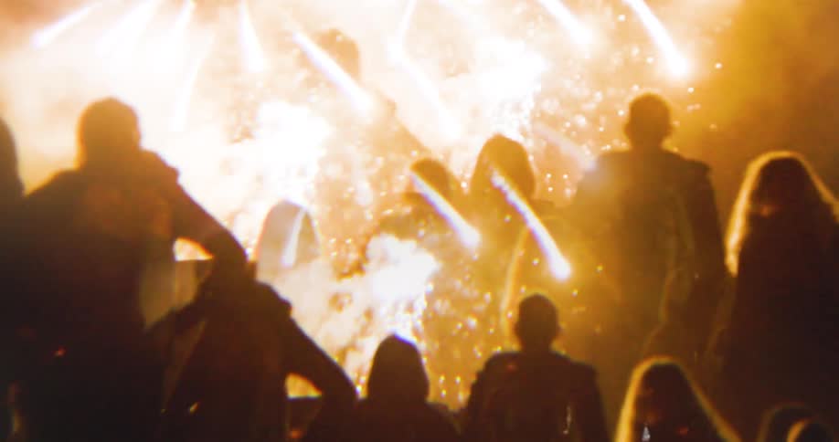 A group of people outdoors at night watches fireworks in the sky illuminating the atmosphere