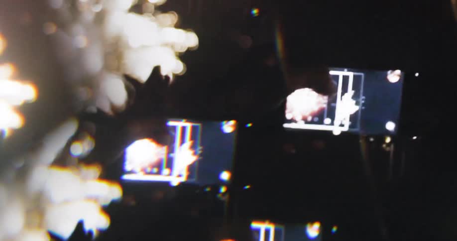 People capturing fireworks on their phones during a nighttime celebration