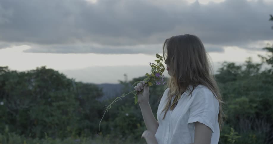 A woman picks up some plant and smells it