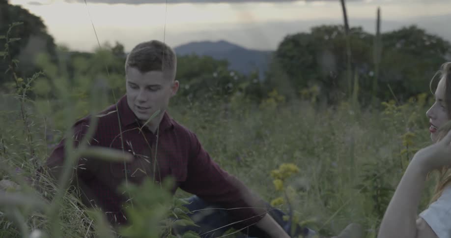 A man and women sit in tall grass together talking