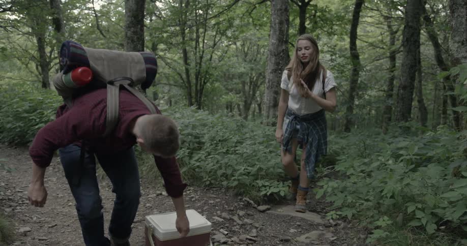 Man tying his boot as his girlfriend approaches in a hiking scene