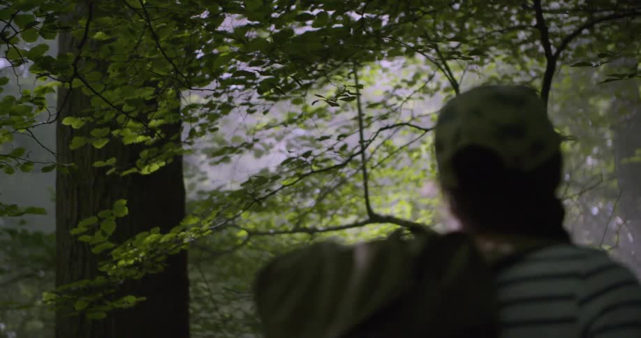 A young woman hiking on a dense forest with a backpack and a baseball cap