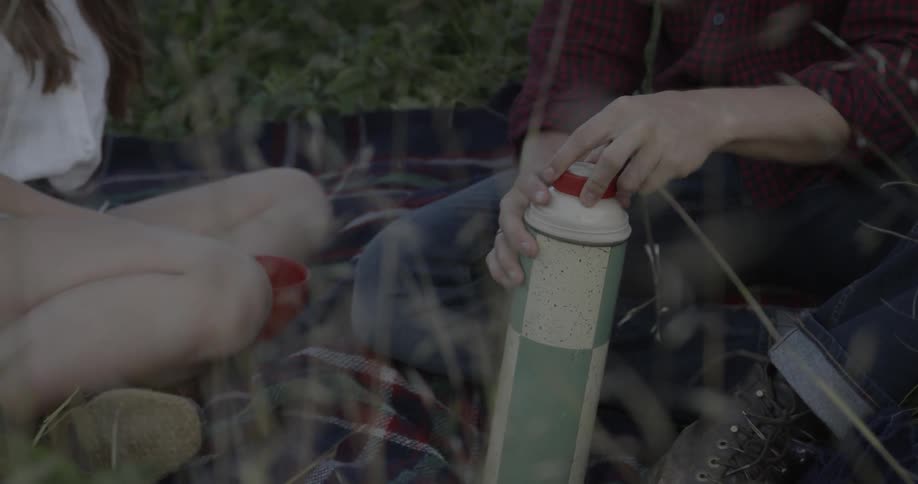 Two people have a picnic and open a thermos