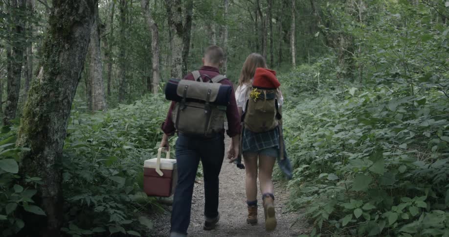 Two people walk with camping equipment down a trail