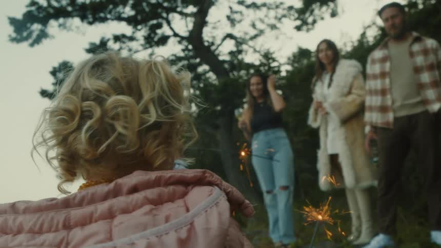 Little girl holding a lit candle and adult people standing outdoors watching