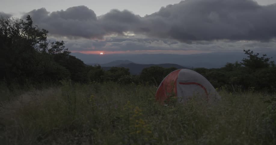A tent is blowing in the wind of this field at dawn