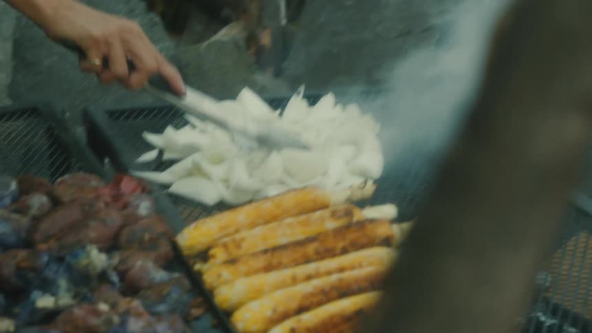 Woman with a spatula roasting vegetables on a grill over an outdoor fire pit