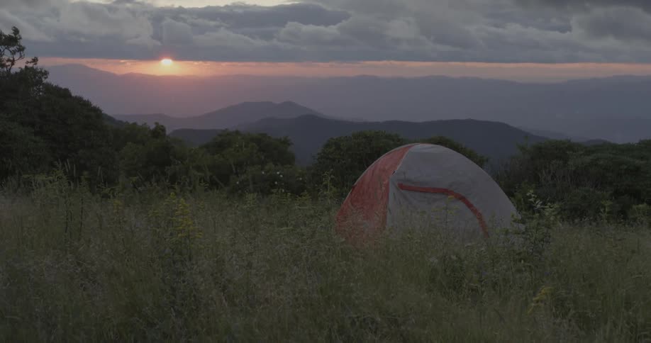 A tent is set in the tall grass at sunset