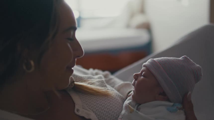New mother lying in a hospital bed smiles at her sleeping newborn