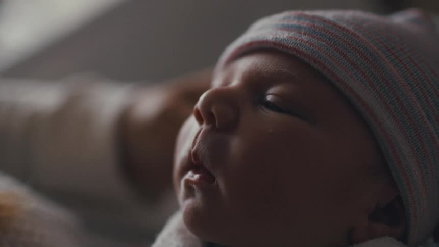 Face of a newborn baby being caressed by the hand of his mother indoors during day time