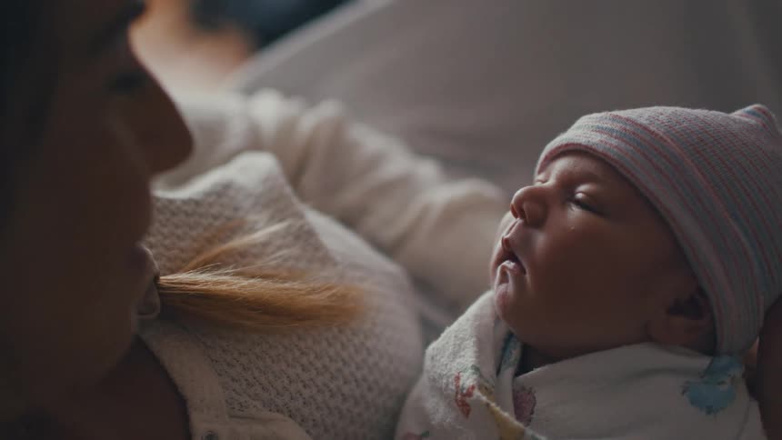 A mother holds an infant wrapped in a blanket and the womans face is close to the infants face