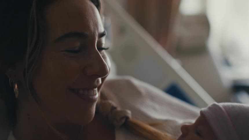 New mother lying in a hospital bed smiles at her newborn