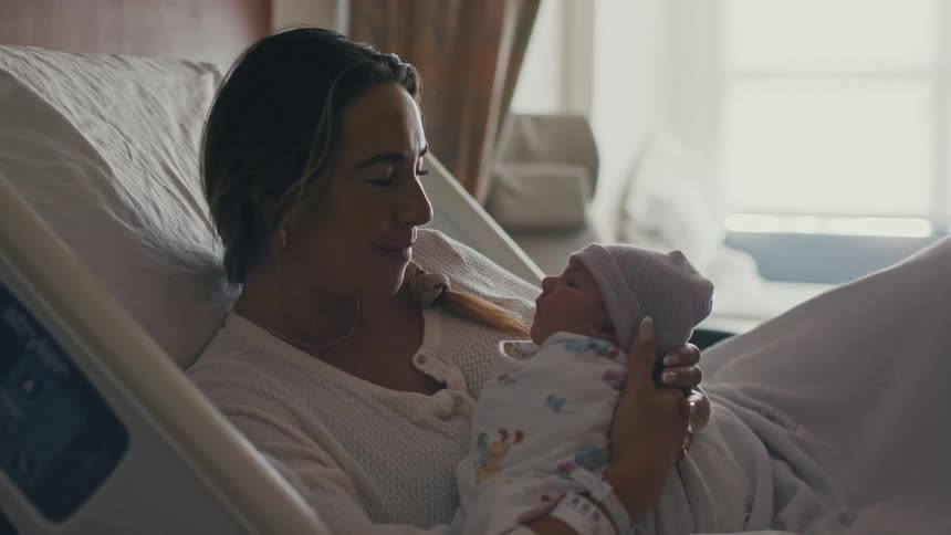 Mother holding newborn baby while lying in a hospital bed