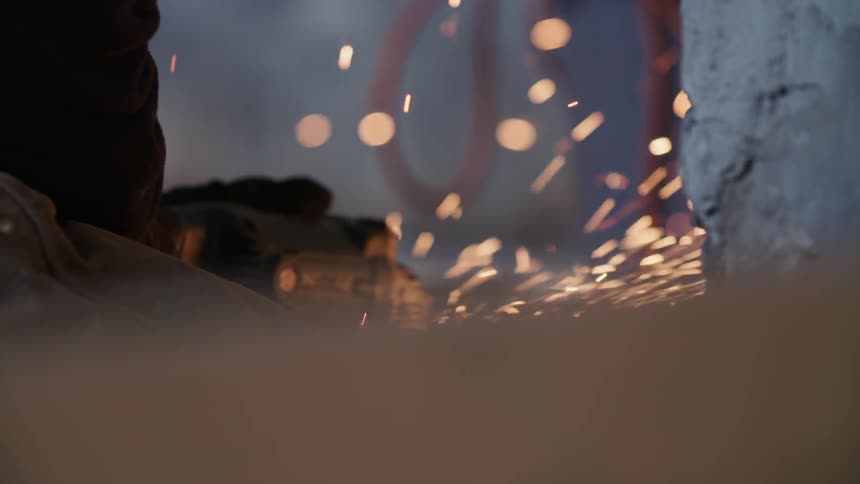 Sparks fly as a man cuts something in a shop