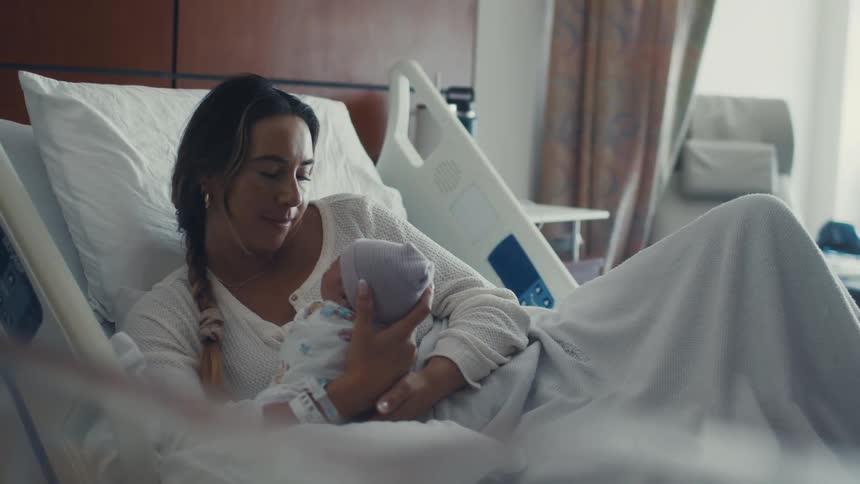 A mother holds her newborn in the hospital bed