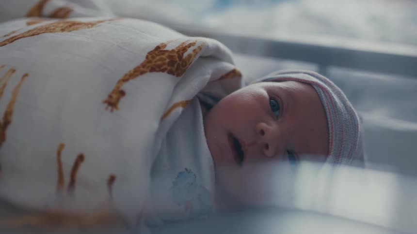A close up view of a cute newborn baby baby is wearing a hat on its head and its is wide awake