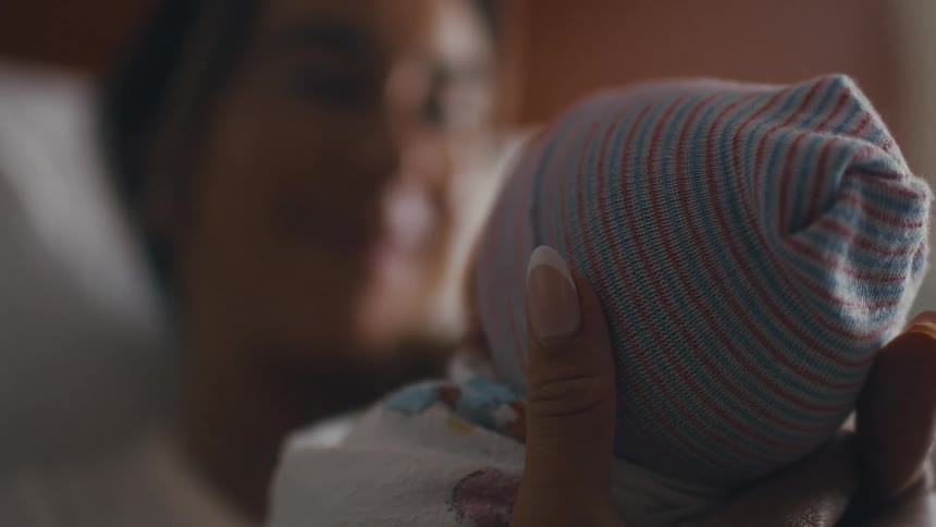 A woman smiles warmly as she cradles a newborn baby in a striped cap close to her face