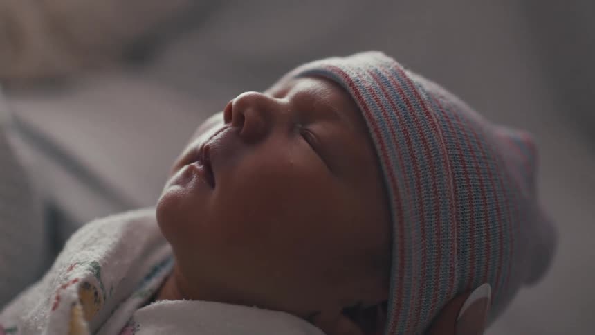 A newborn baby wearing a striped cap sleeps peacefully wrapped in a blanket