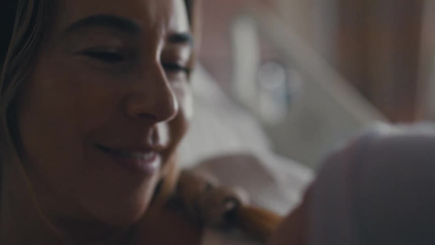 A mother lies in a hospital bed holding her newborn baby she smiles down at the baby a look of pure joy and adoration on her face