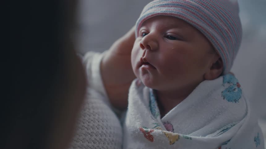 A person holds an infant who is wrapped in a blanket with a beanie on its head