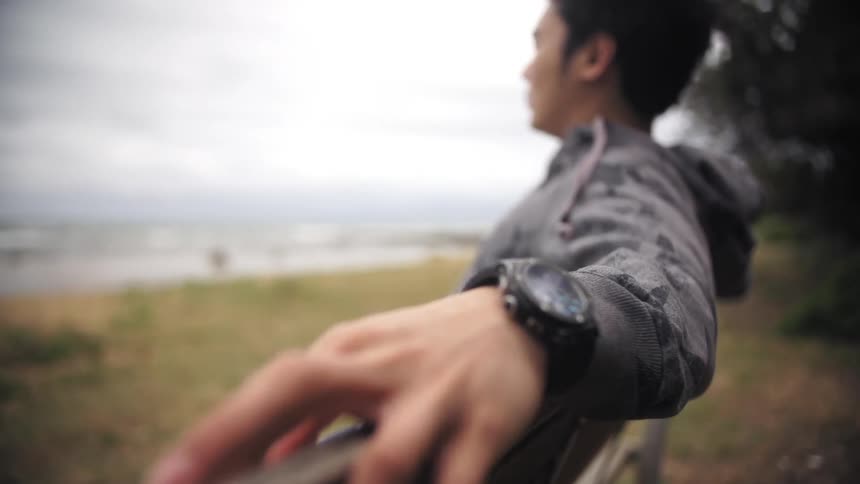A young, asian man sitting on a bench gazing towards the horizon