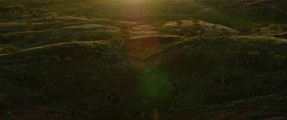 Sun sets over hills covered with vegetation and scattered trees