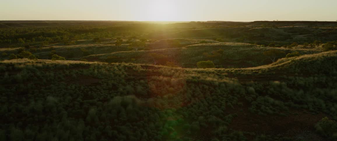 The camera moves slowly above a landscape of hills with the sun setting behind them