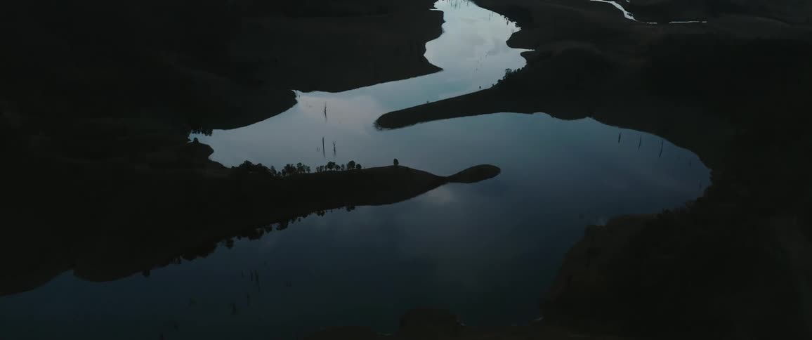 A winding river glistens in the fading light cutting through dark rolling hills