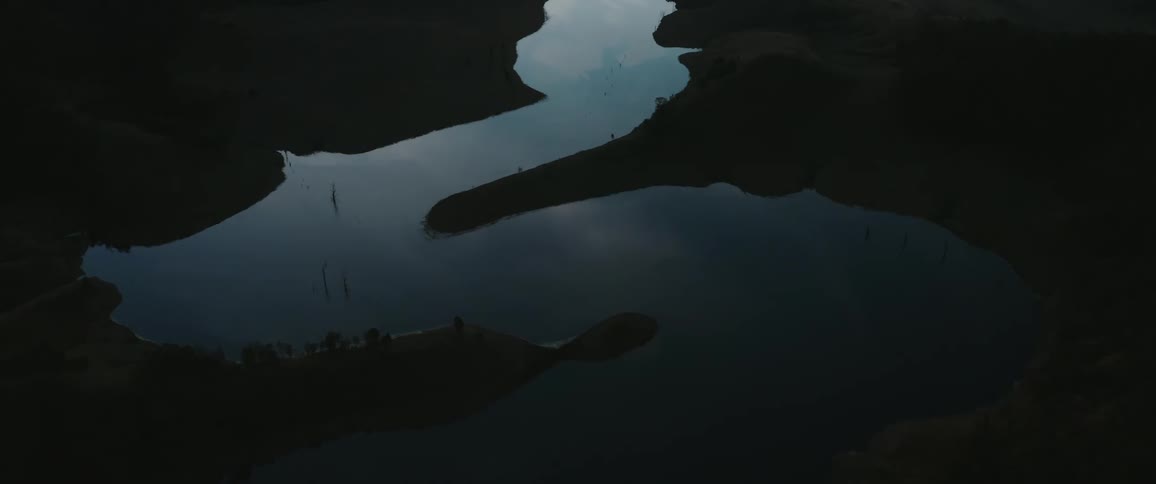 An overhead view shows a body of water with land and trees on its banks