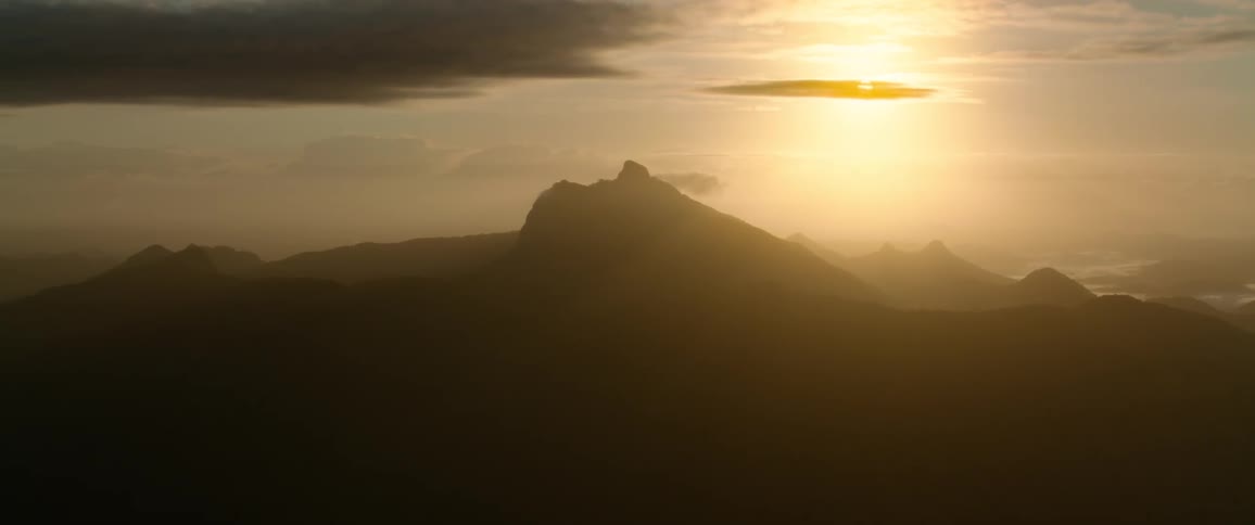 Sun shining in the red sky casts the mountains in a mountain range into silhouette