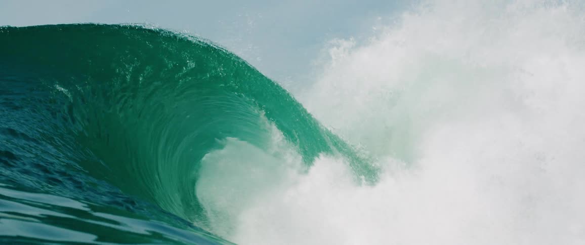 Huge waves rise in the sea crashing down and creating a massive splash under the bright midday sun