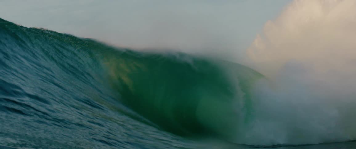 A huge powerful ocean wave with a large crest of foam rolls and breaks with the suns light filtering through the clear turquoise water