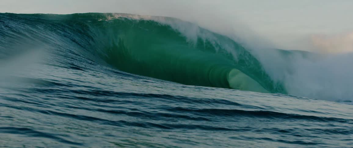 Giant wave rises in the ocean with its white crest spreading through the air