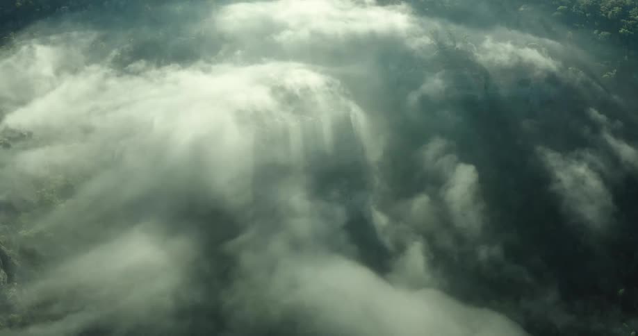 Sunlight streams through a swirling sea of mist and clouds above a dense dark forest