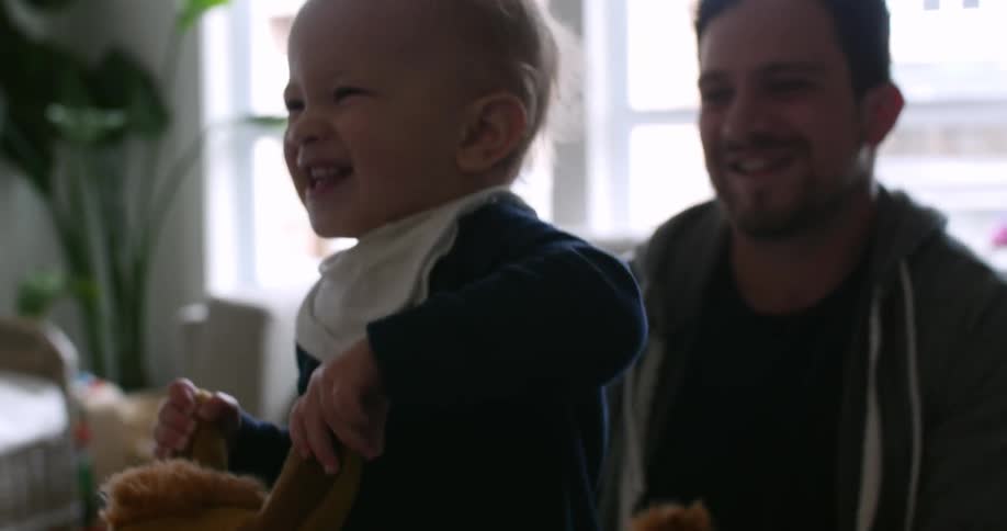 Baby smiles as he hops on a toy with smiling man behind him