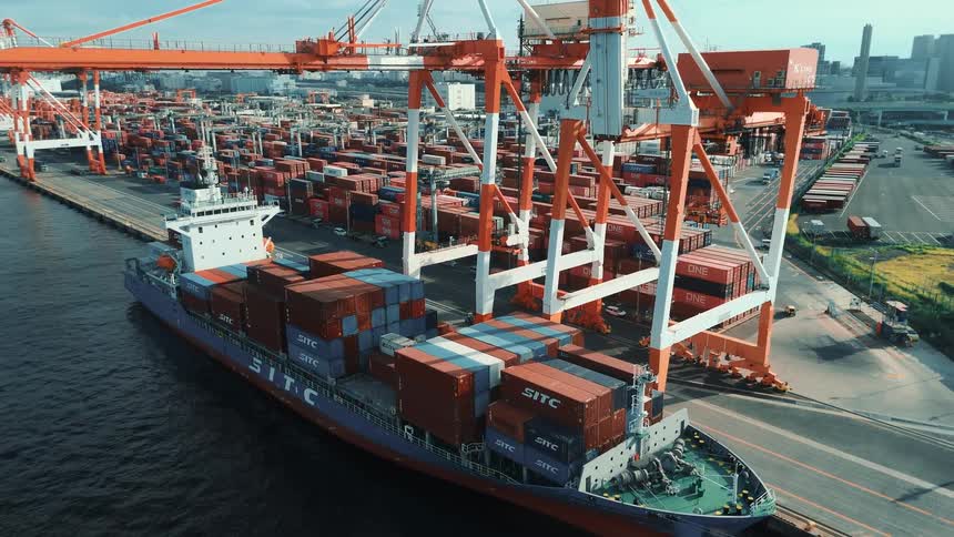 A busy seaport at midday packed with towering stacks of colorful cargo containers as trucks loaded with container freight drive in and out along the paved lanes under the bright sun