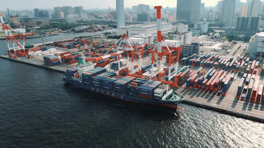 A crane filling a cargo boat with shipping containers on a commercial port with a container depot