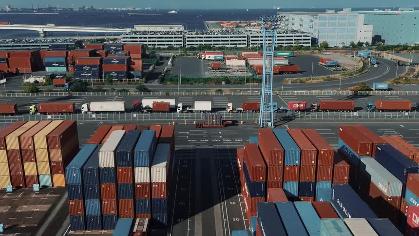 A bustling seaport at midday filled with towering stacks of cargo containers tarred roads weave through the port linking different sections as trucks move to and fro hauling containers under the bright sun