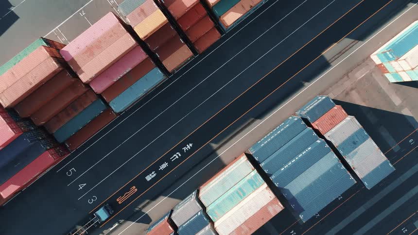 A lone truck drives through a terminal yard between immense stacks of colorful shipping containers