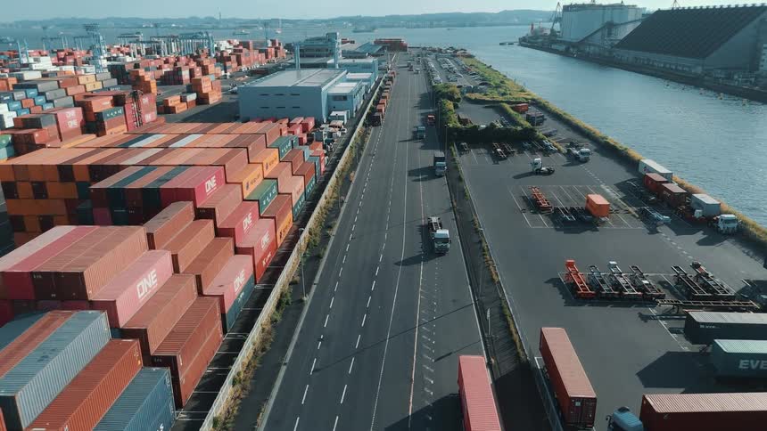 Aerial view of a shipping yard with stacked cargo and trucks near a lake