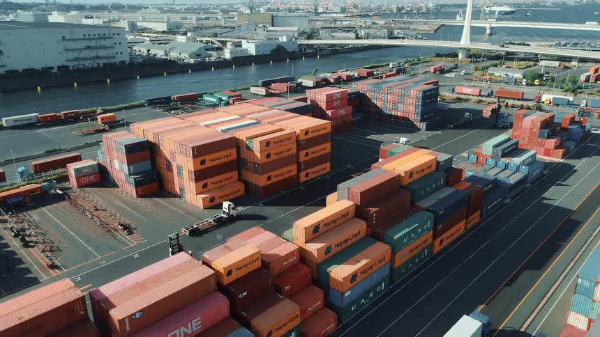 A massive shipping container yard with stacks of colorful containers neatly arranged along a waterfront as trucks move about the busy terminal