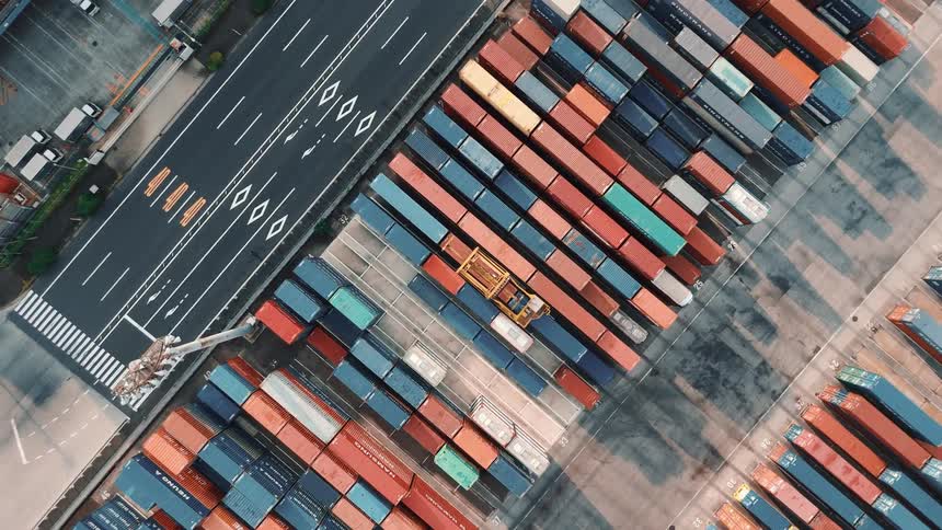 A busy container port with stacked colorful containers a roadway and a yellow gantry crane moving across the yard
