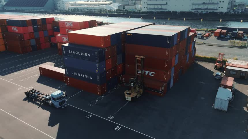 A forklift moves shipping containers in a storage yard near the docks with stacks of colorful containers organized in rows