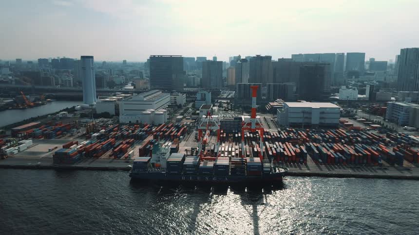 Cargo ship docked at a port full of containers in front of urban buildings