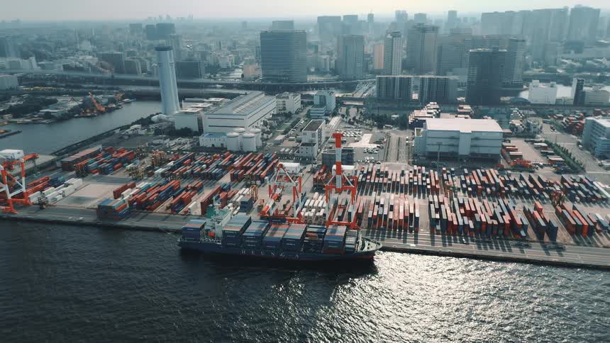 Freight ship full of containers docked on a port with a metropolitan area on the background outdoors during day time