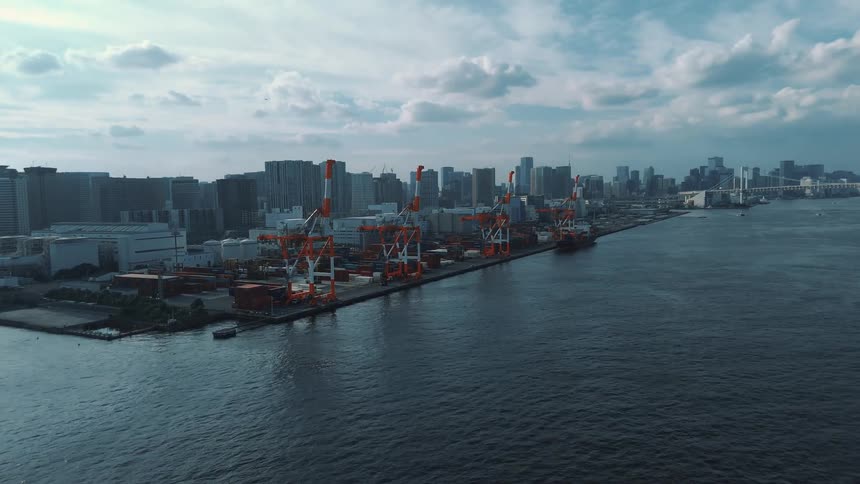Orange cranes and aligned containers at a port facing the city