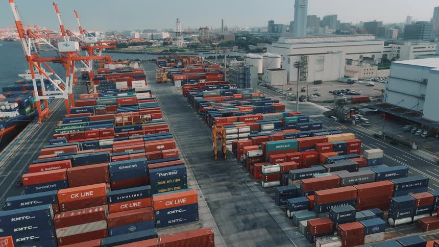 A bustling seaport at midday filled with stacks of colorful cargo containers in the harbor a cargo ship loaded with containers sits docked while a towering crane hovers above the city skyline rises in the background