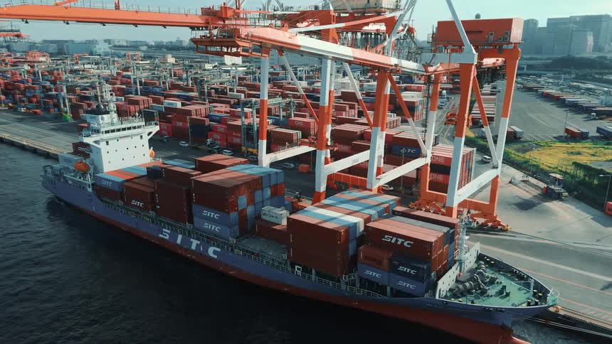 Cranes loading up a cargo ship with shipping containers on a port with a large container depot