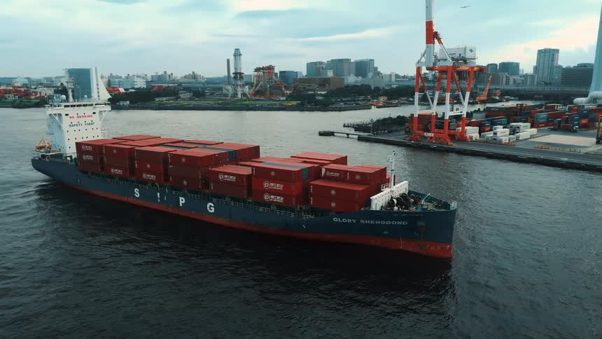 Cargo ship carries red containers near the port with cranes